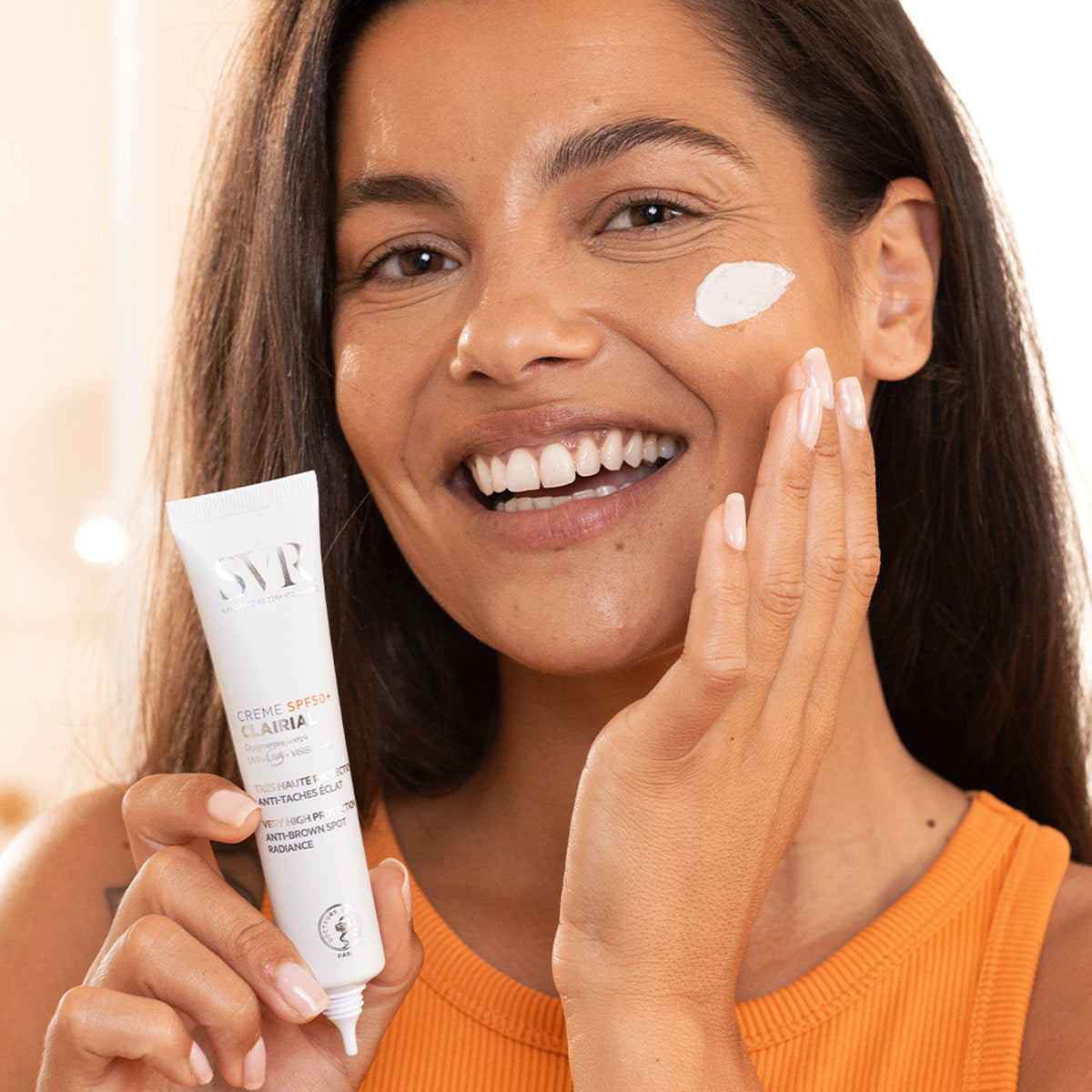 Femme souriante appliquant la crème SVR Clairial SPF50+ blanche sur son visage pour traiter les taches brunes.