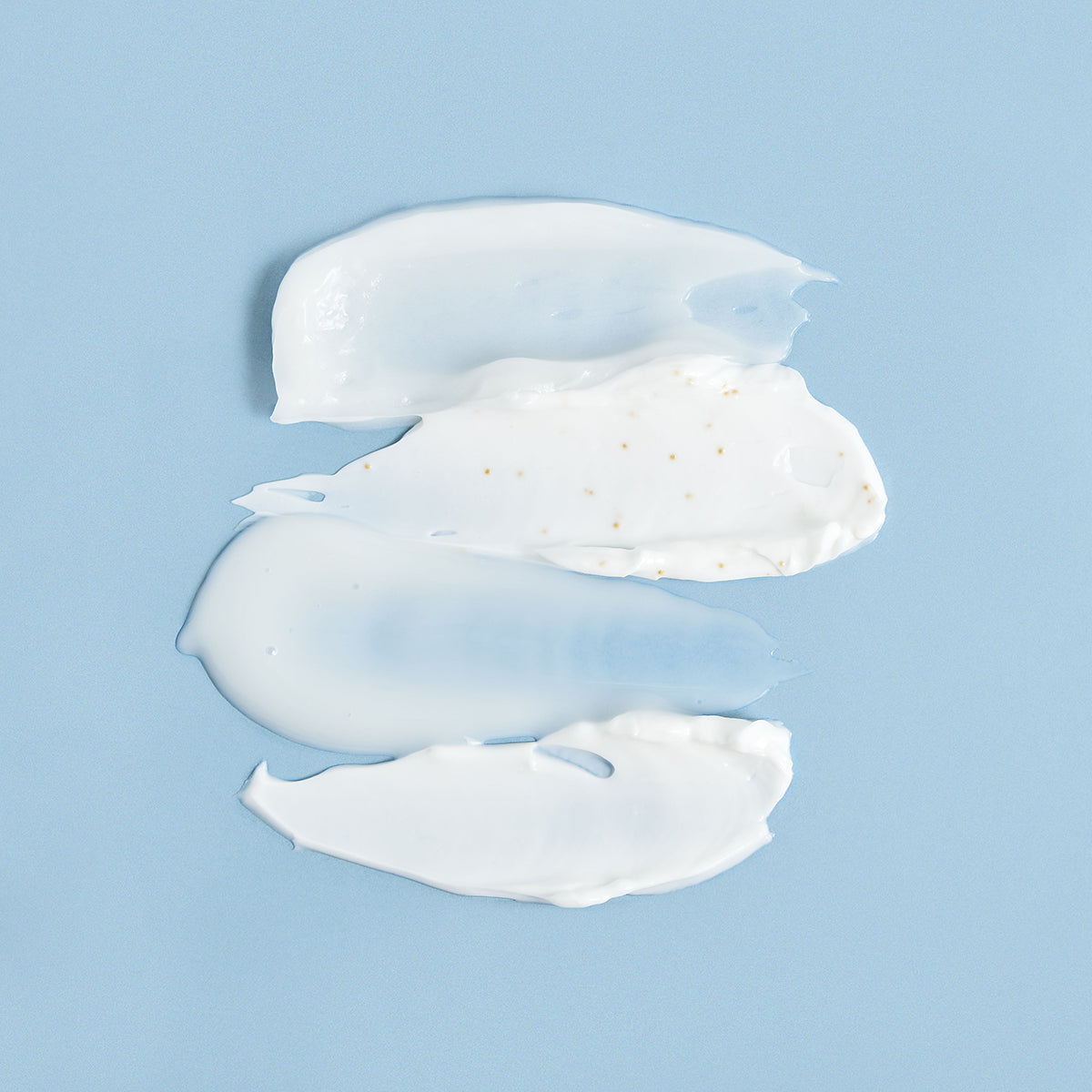 Trois textures de crème blanche onctueuses et un gel translucide étalés sur un fond bleu clair.