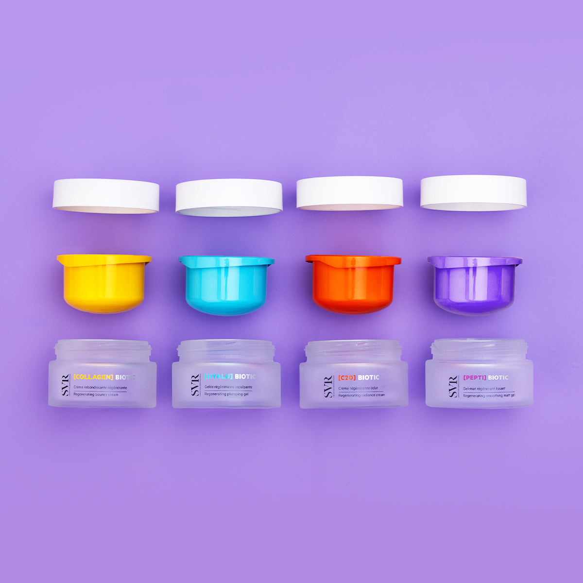 Quatre pots de crème SVR Biotic avec couvercles blancs et inserts colorés jaune, bleu, orange et violet sur fond lilas.