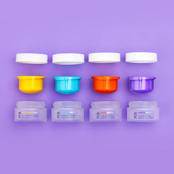 Quatre pots de crème SVR Biotic avec couvercles blancs et inserts colorés jaune, bleu, orange et violet sur fond lilas.