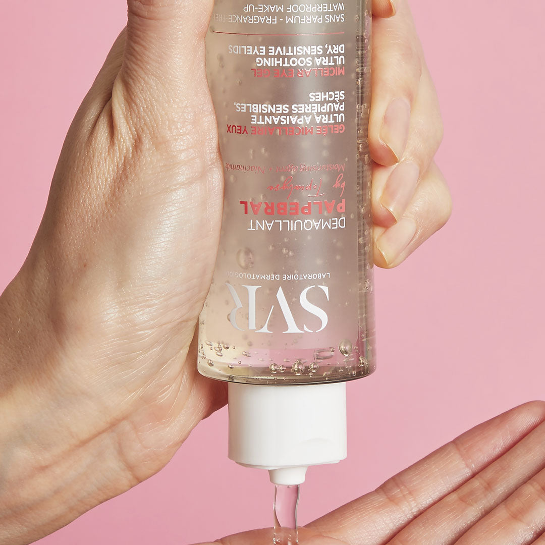 Main tenue par une main versant le gel démaquillant SVR Palpebral sur une paume, sur fond rose.