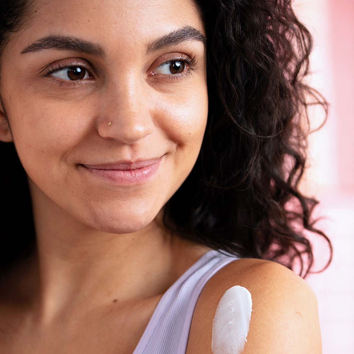 Femme souriante avec une texture de crème blanche nourrissante appliquée sur l'épaule pour hydrater sa peau sensible.