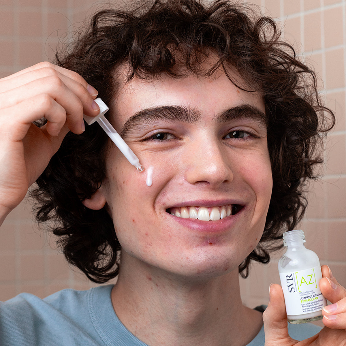 Jeune homme souriant appliquant le sérum SVR Sebiaclear Ampoule Flash avec une pipette sur sa peau à tendance acnéique.