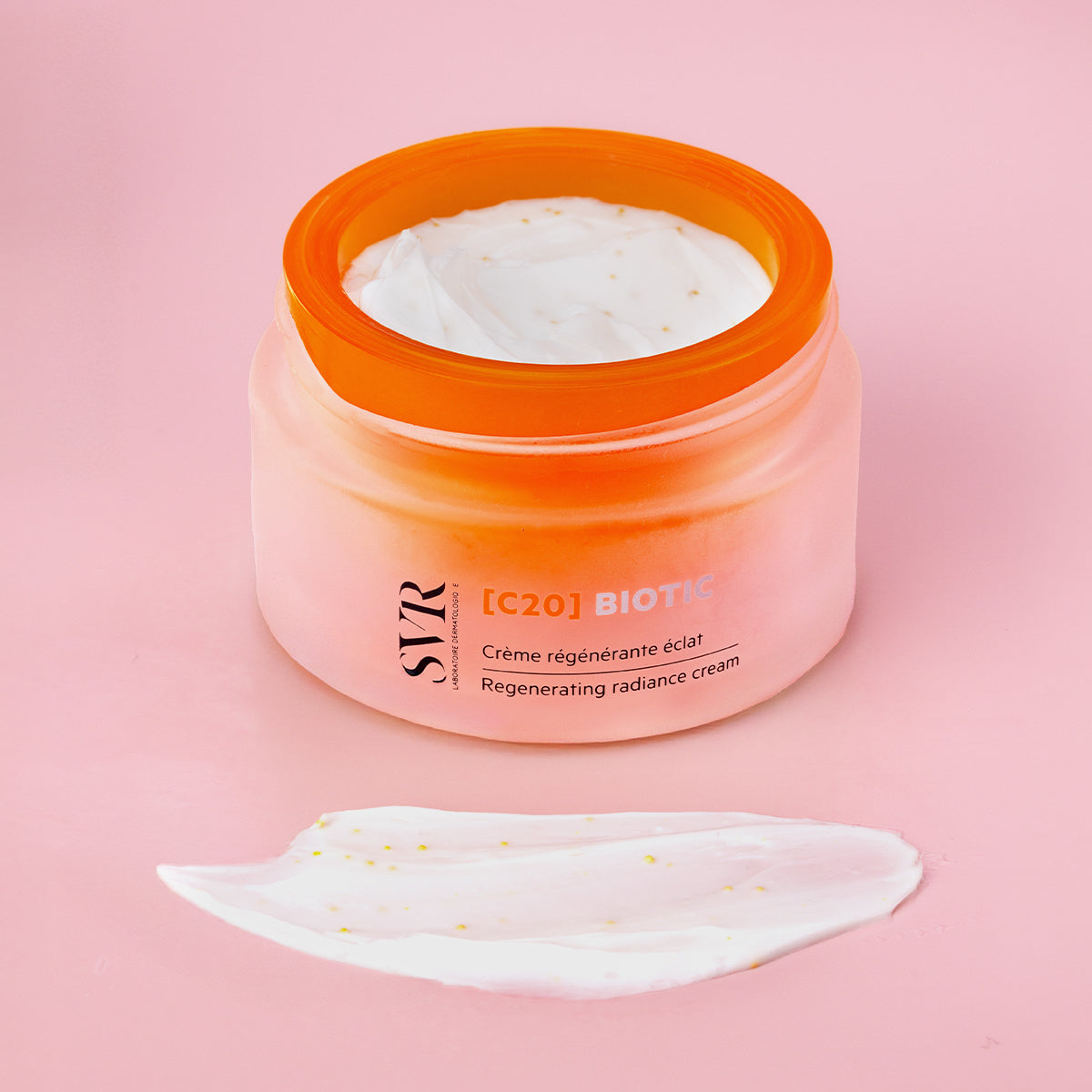 Pot de crème SVR [C20] Biotic en verre dépoli orange avec couvercle vif et texture onctueuse sur fond rose.